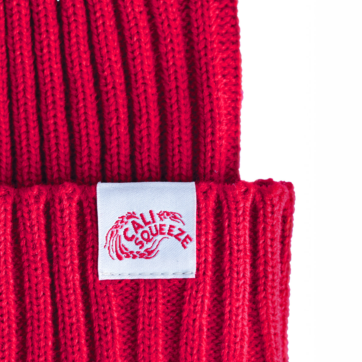 Close-up of the white woven Cali Squeeze label on the cuff of the red Cali Squeeze Logo Beanie
