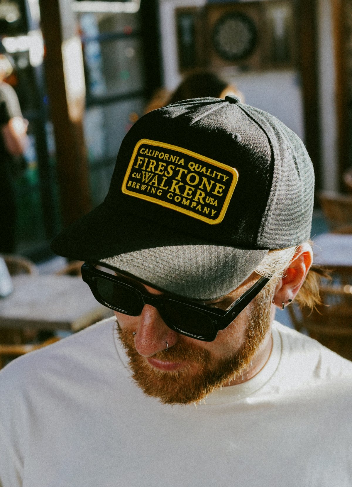 Man in sunglasses wearing a black Firestone Walker hat with a gold patch and cream Firestone Walker tee