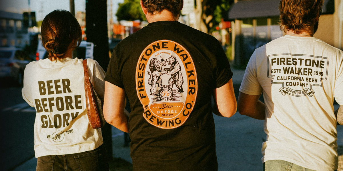 Three friends walking down a sidewalk, seen from behind, wearing a cream Firestone Walker Beer Before Glory tee, a black Firestone Walker crest tee, and a cream Firestone Walker California Beer Company tee.