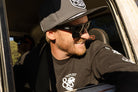 Man wearing 805 x Heat Wave Vise sunglasses, cap, and 805 x Heat Wave long sleeve shirt, smiling in an off-road vehicle
