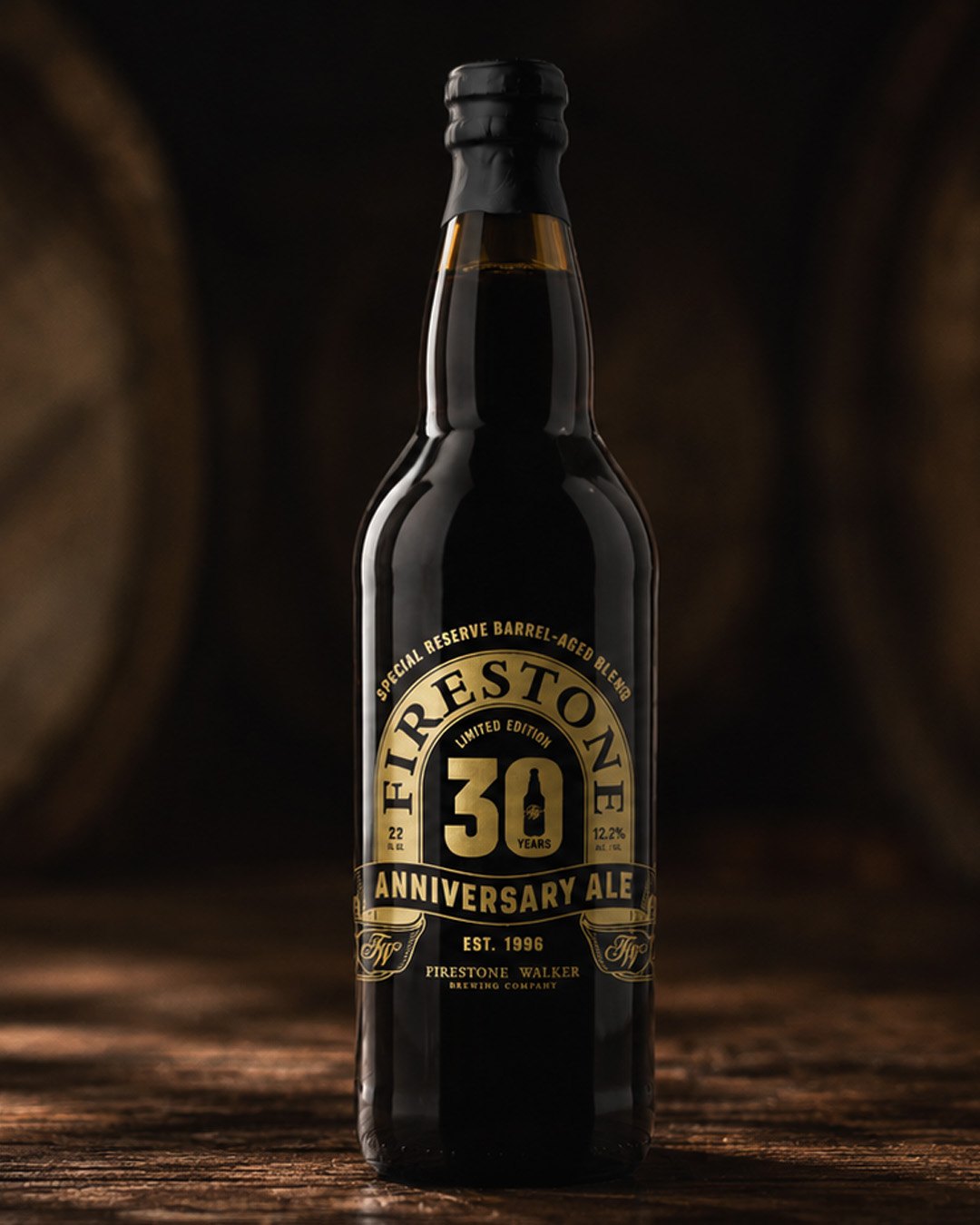 Bottle of Firestone Walker 30 Years Anniversary Ale with a black and gold label, on a wooden table in a dim barrel room