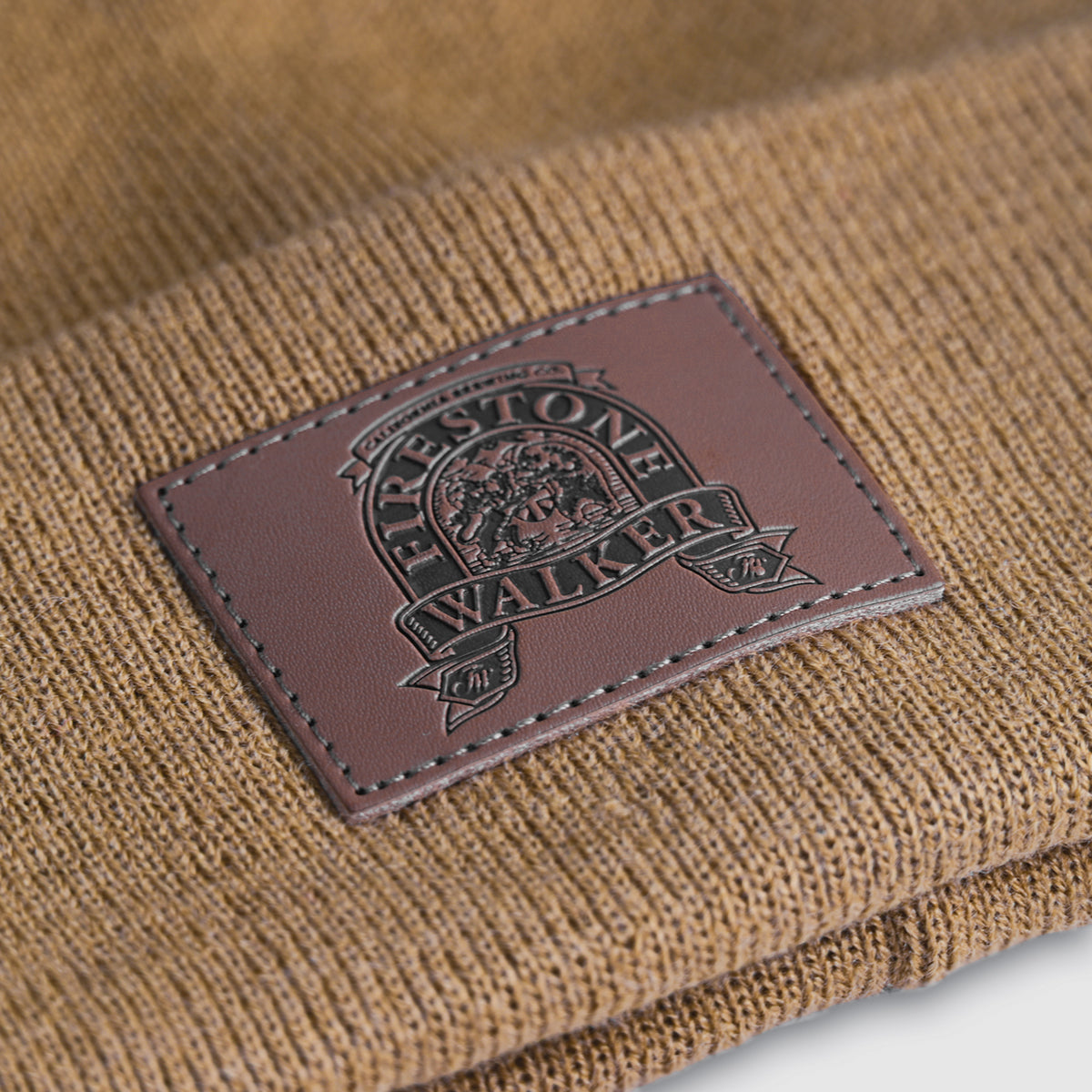 Close-up of Firestone Walker leather patch with stitched edges on tan knit beanie cuff